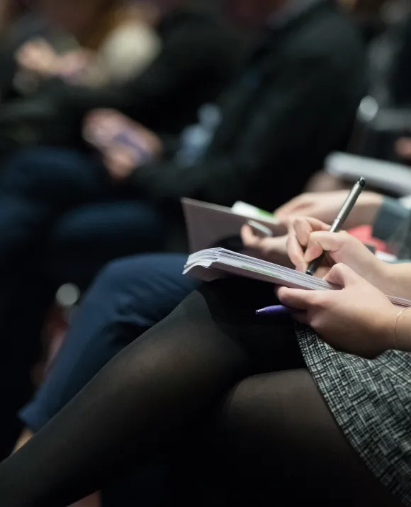 Person writing on a notepad while seated with legs crossed